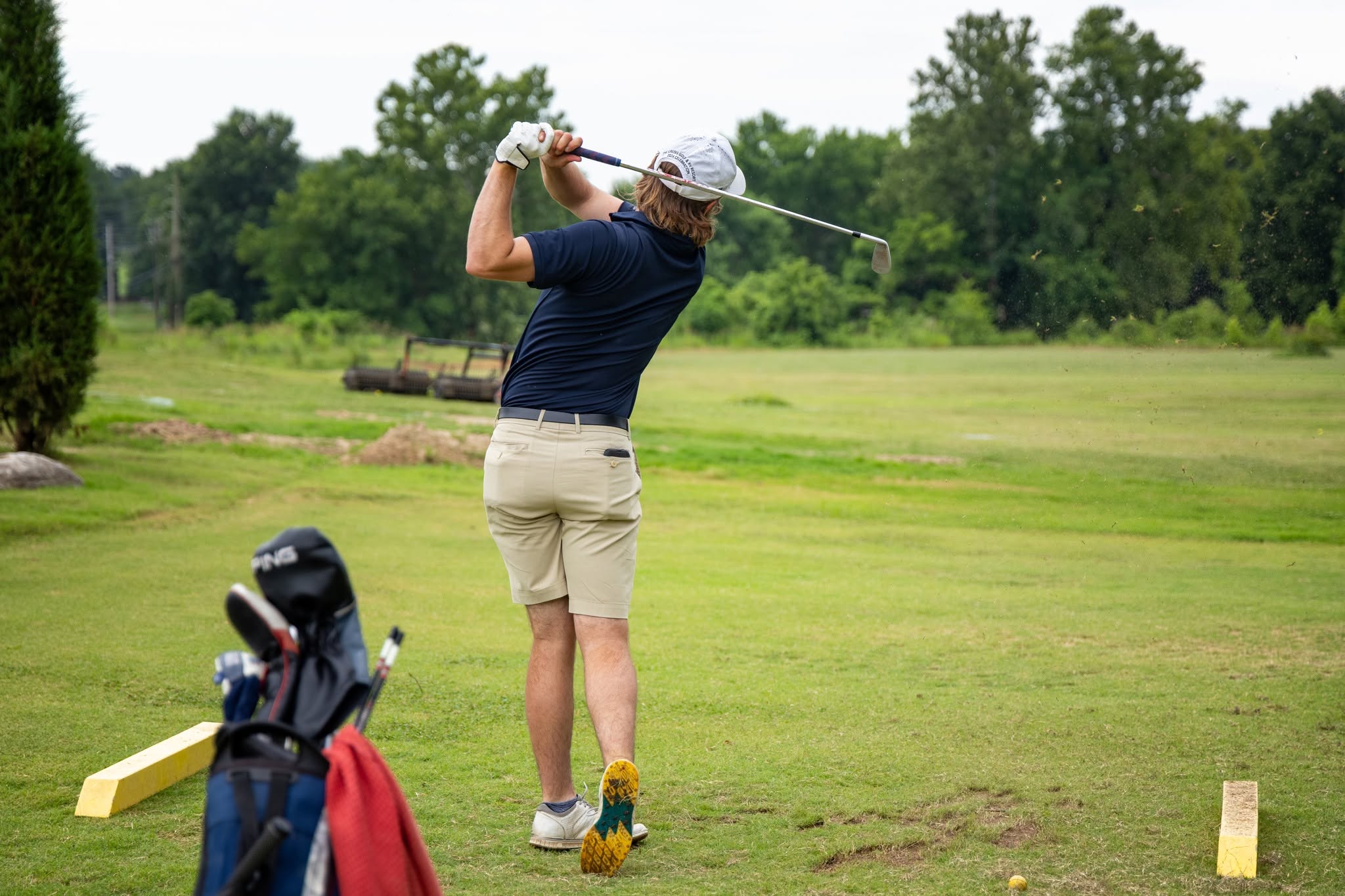 A golfer at the top of an iron swing with a bag beside the tee at The Creeks