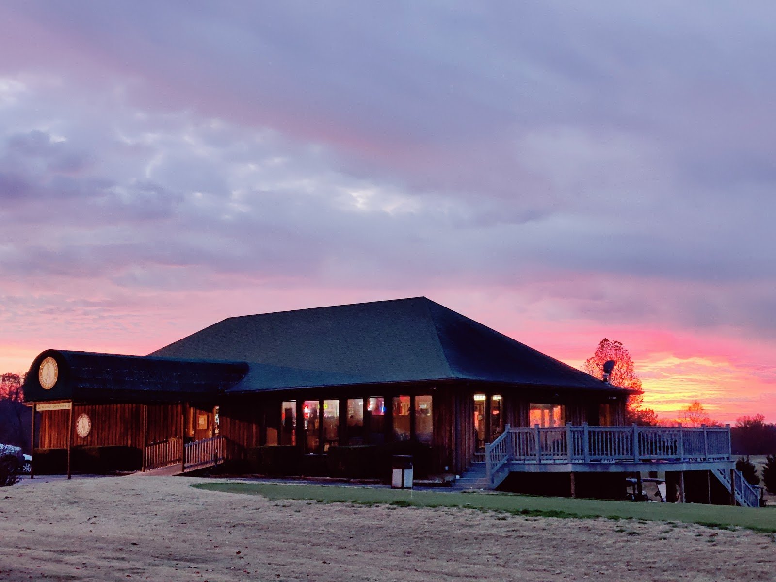 The Creeks clubhouse at dusk, windows glowing gold beneath a pink Ozark sunset